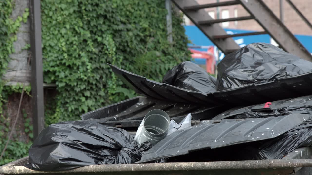 contenedor de basura desbordante con montones de bolsas de basura de plástico negro