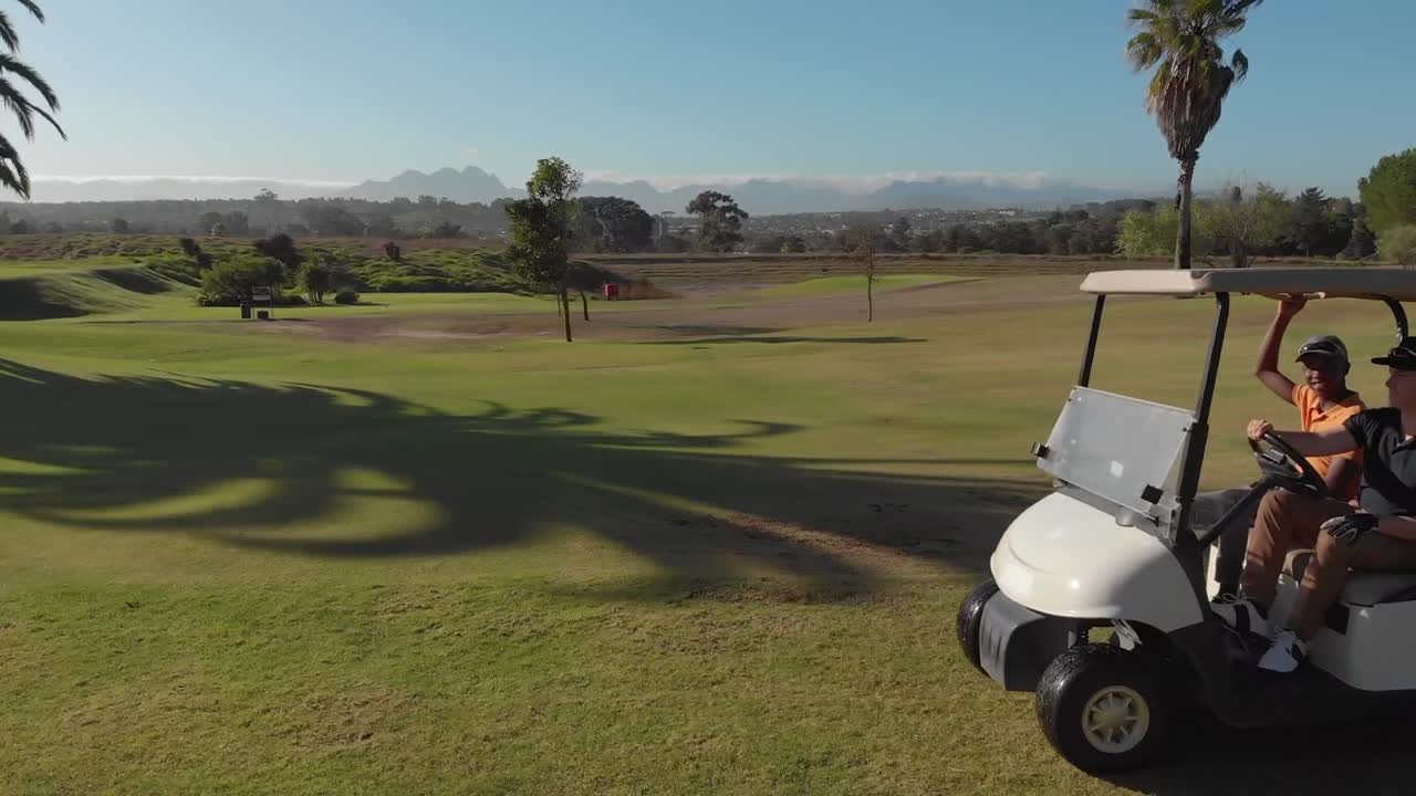 Kaksi eri taustaista miesgolfaajaa ajamassa golfautoa golfkentällä aurinkoisena päivänä