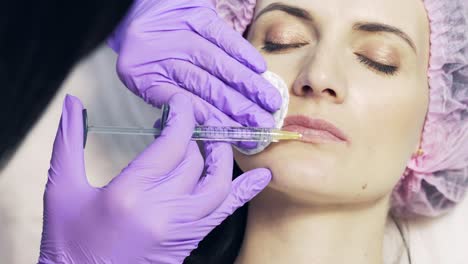 cosmetician makes an injection of hyaluronic acid in a beautiful lips and dries with cotton in beauty salon