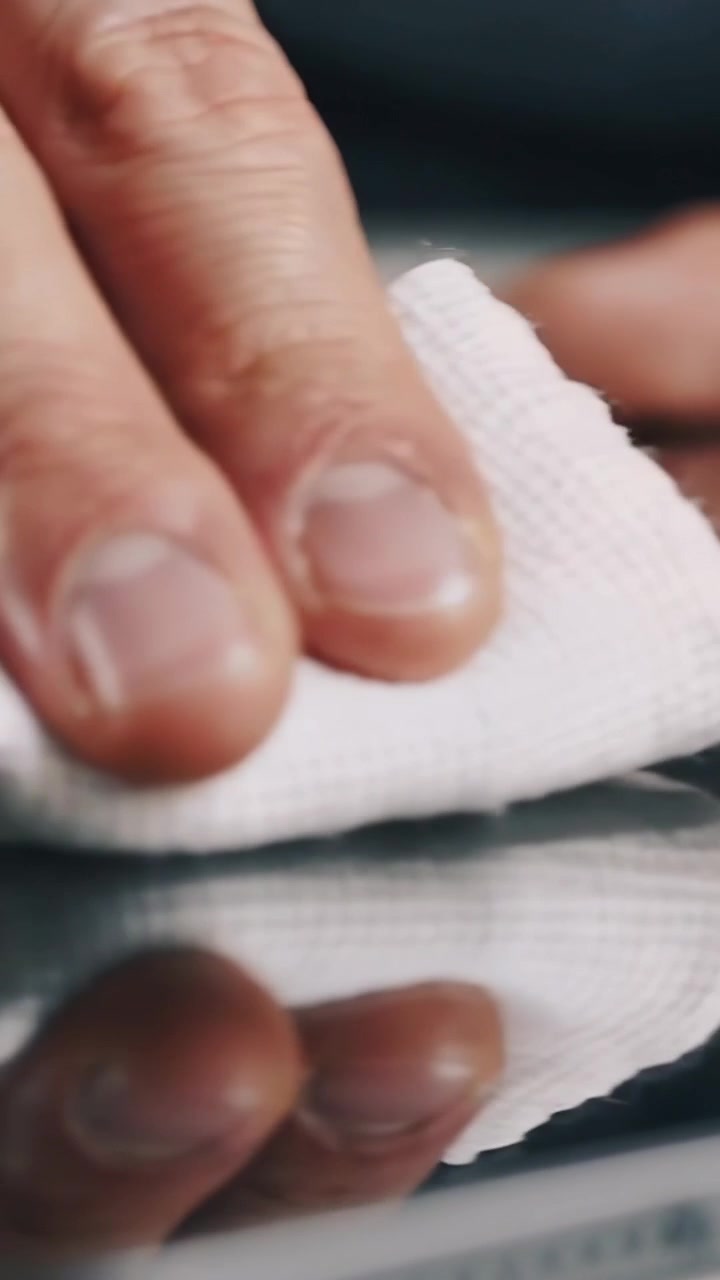 Vertical video: Wiping male hand pressing white cloth across glass screen at desk, removing streaks