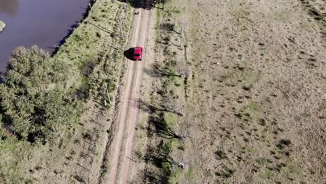 aerial shot of green countryside and red car driving through