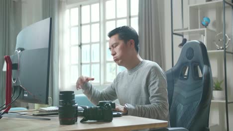 asian cameraman in long sleeved t-shirt being tired while using desktop computer for working at home.