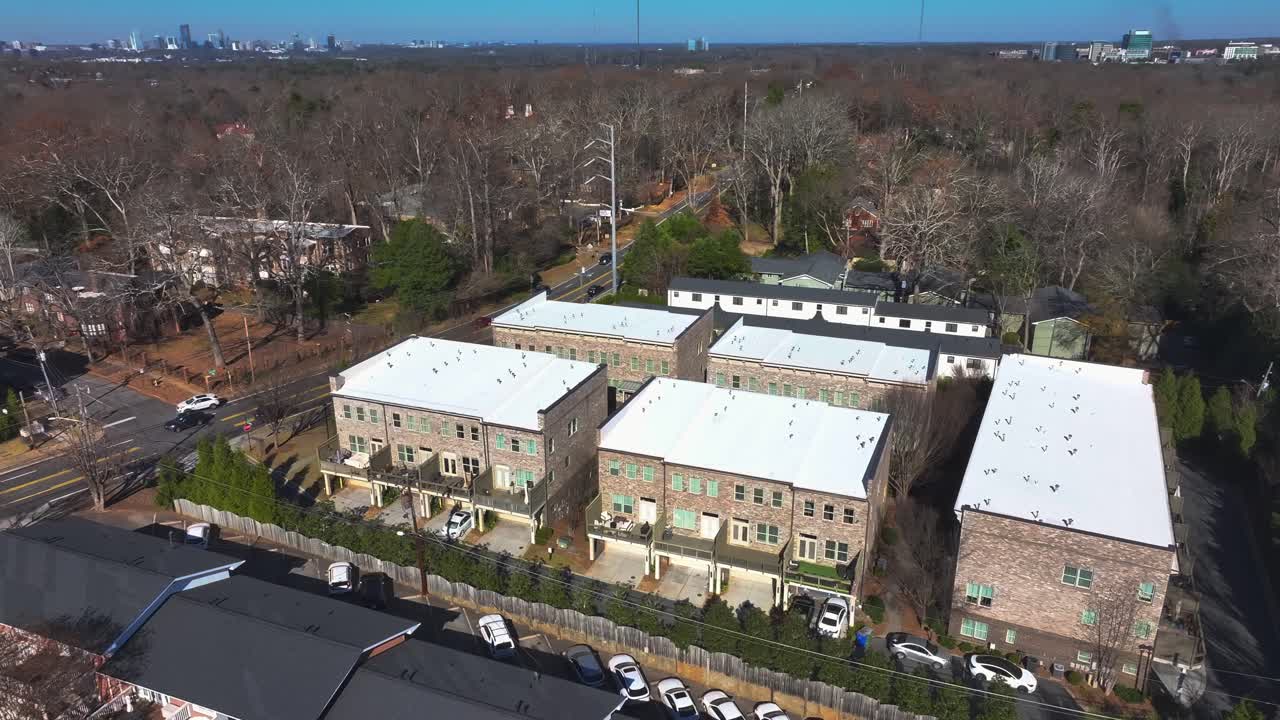 Aerial view of Apartment houses in Suburb of american town. Sunny day in winter season. Driving cars on main street. Brick style homes. Atlanta Downtown in Background. Wide shot.