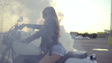 young woman sitting on a motorcycle doing a tire burnout. pretty female biker in shorts sitting on the motorcycle seat in smoke