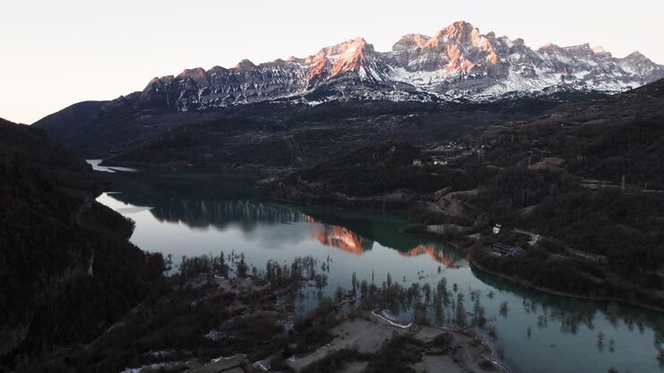 Alba su cime montuose innevate e un lago alpino tranquillo.