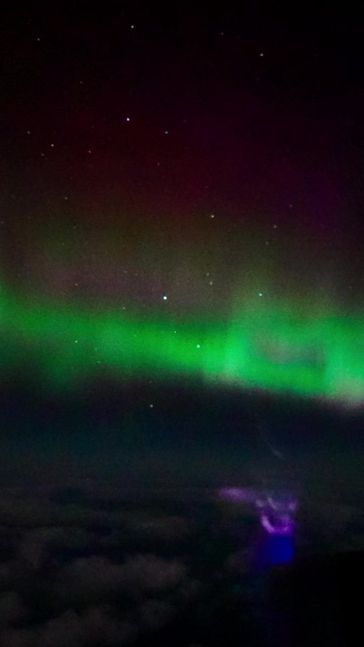 Fantastisk vertikalt bilde av det grønne nordlyset som skimrer over skyer, fanget fra høy høyde under en nattflyvning. Unikt perspektiv av nordlyset og stjernehimmelen