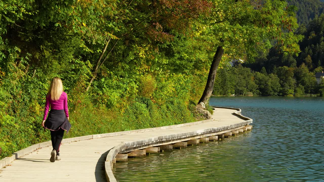 Donna che cammina lungo il sentiero del lago di Bled circondata da una foresta verde, statica media vista posteriore