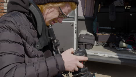 close up view of redheaded production worker in wool cap and sunglasses setting up a camera in the street 1