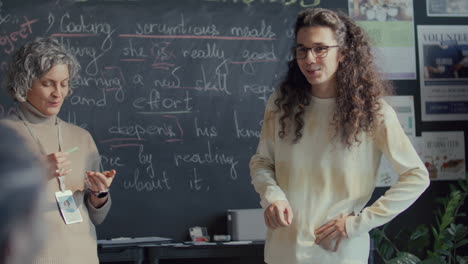 student standing at blackboard, talking to teacher and peers in english class