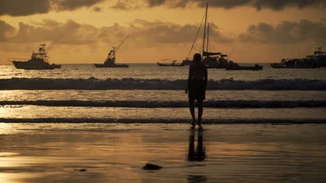 beach silhouette of someone walking over the beach with her feet in the ocean of playa tamarindo, costa rica