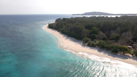 descending aerial shot of crashing waves on sea shore of gili meno island