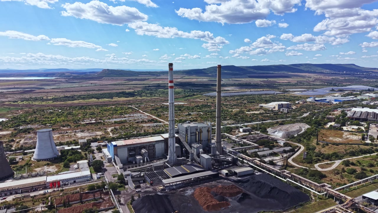 Vista de central eléctrica con torres de refrigeración y chimeneas en un paisaje rural bajo un cielo azul con nubes