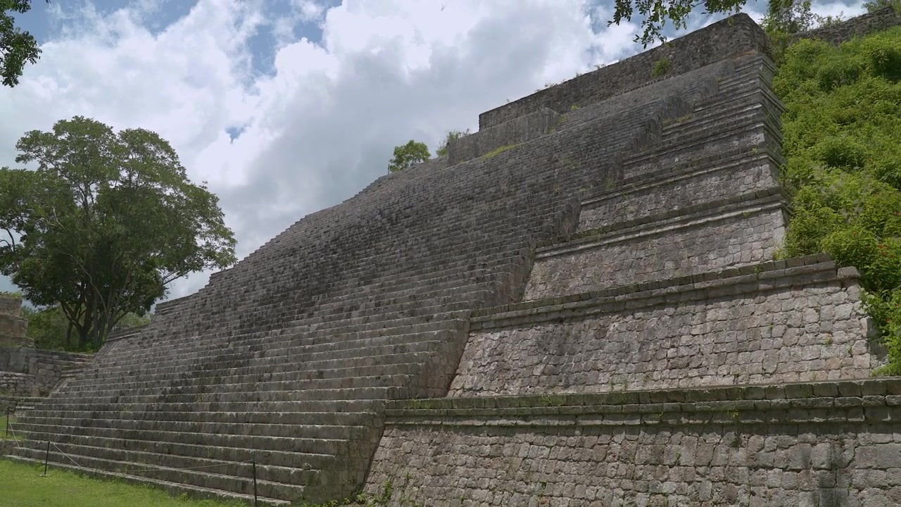 Inquadratura grandangolare statica dal basso delle massicce scale piramidali in pietra e dei livelli a gradoni presso il sito archeologico di Edzná a Campeche, Messico.