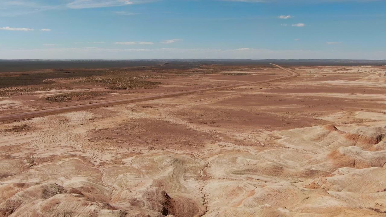 Uma vasta extensão de terreno desértico árido estende-se pelo horizonte com uma estrada de terra que o atravessa em Wyoming. Ideal para projetos sobre paisagens remotas ou documentários ambientais