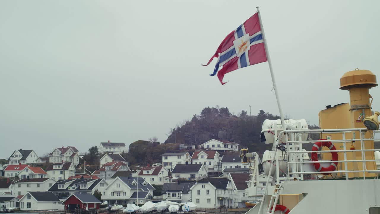 Panoramisk etableringsbilde med et norsk splittflagg med riksskjoldet i midten, trehus i bakgrunnen, Kragerø, Norge, på en overskyet dag
