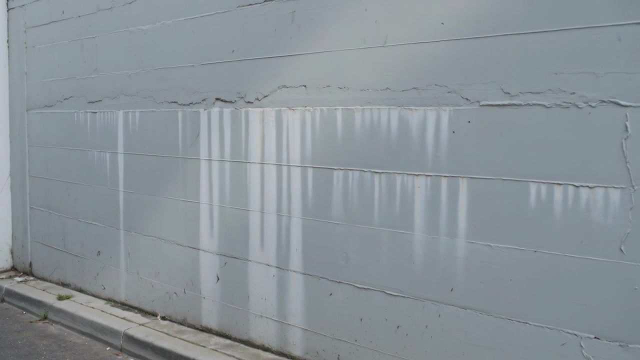 Panning camera moving right on narrow street to reveal painted block wall with pale drips