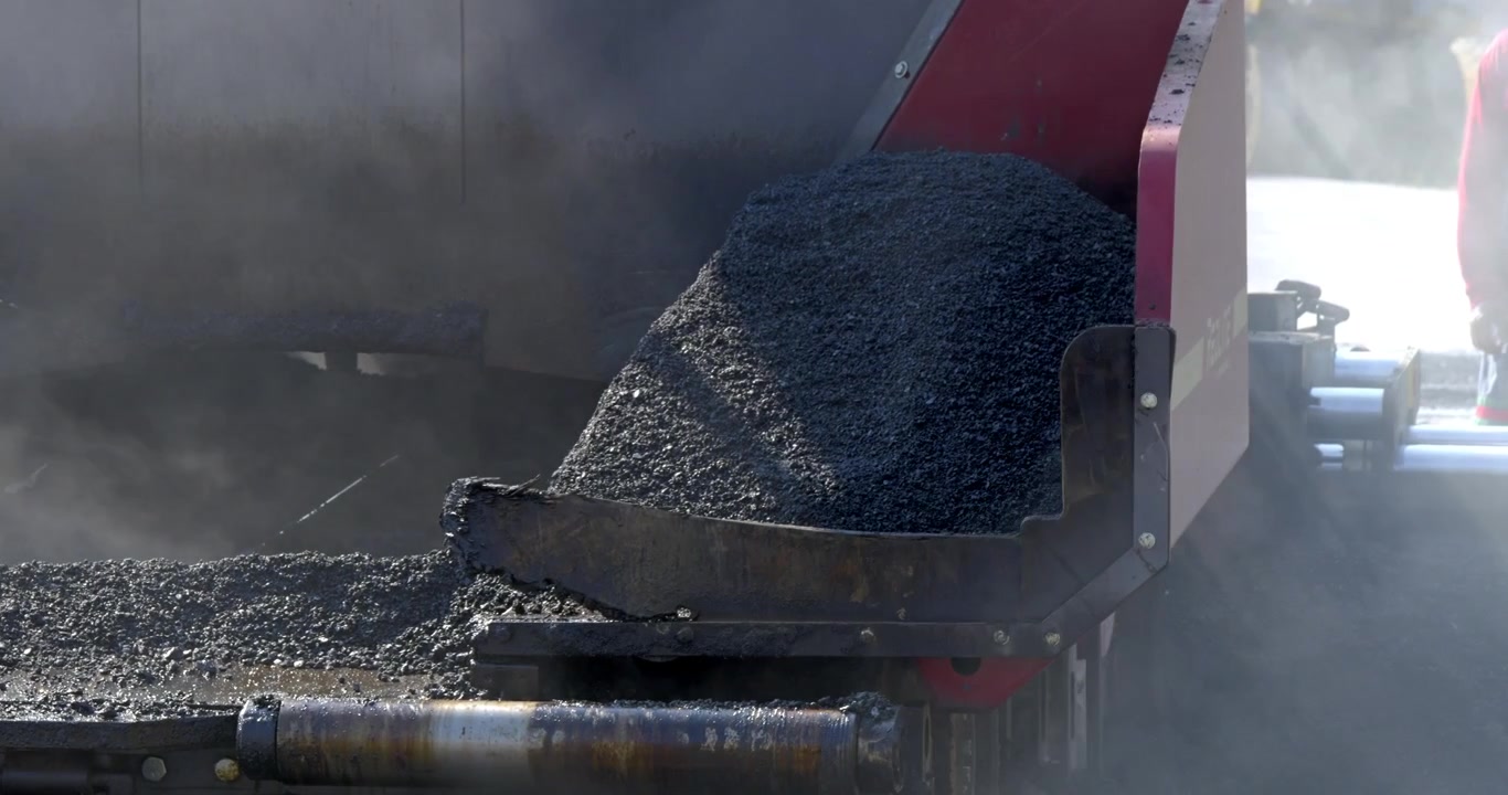A close-up view of asphalt being produced in a construction setting showcasing heavy machinery in action.