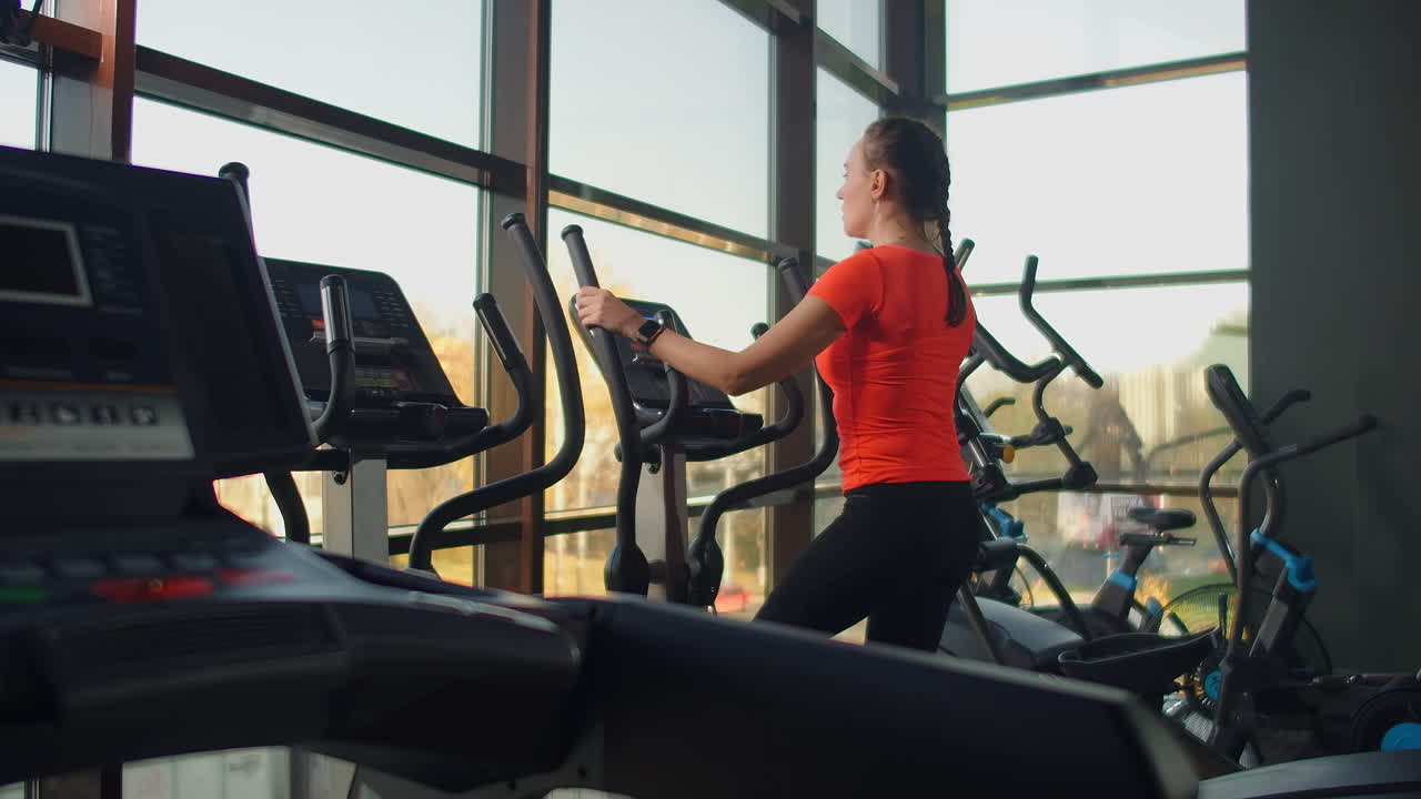 Beautiful fit sportive positive young woman in gym doing exercises on elliptical trainer working out. Slow motion the woman on the elliptical trainer.