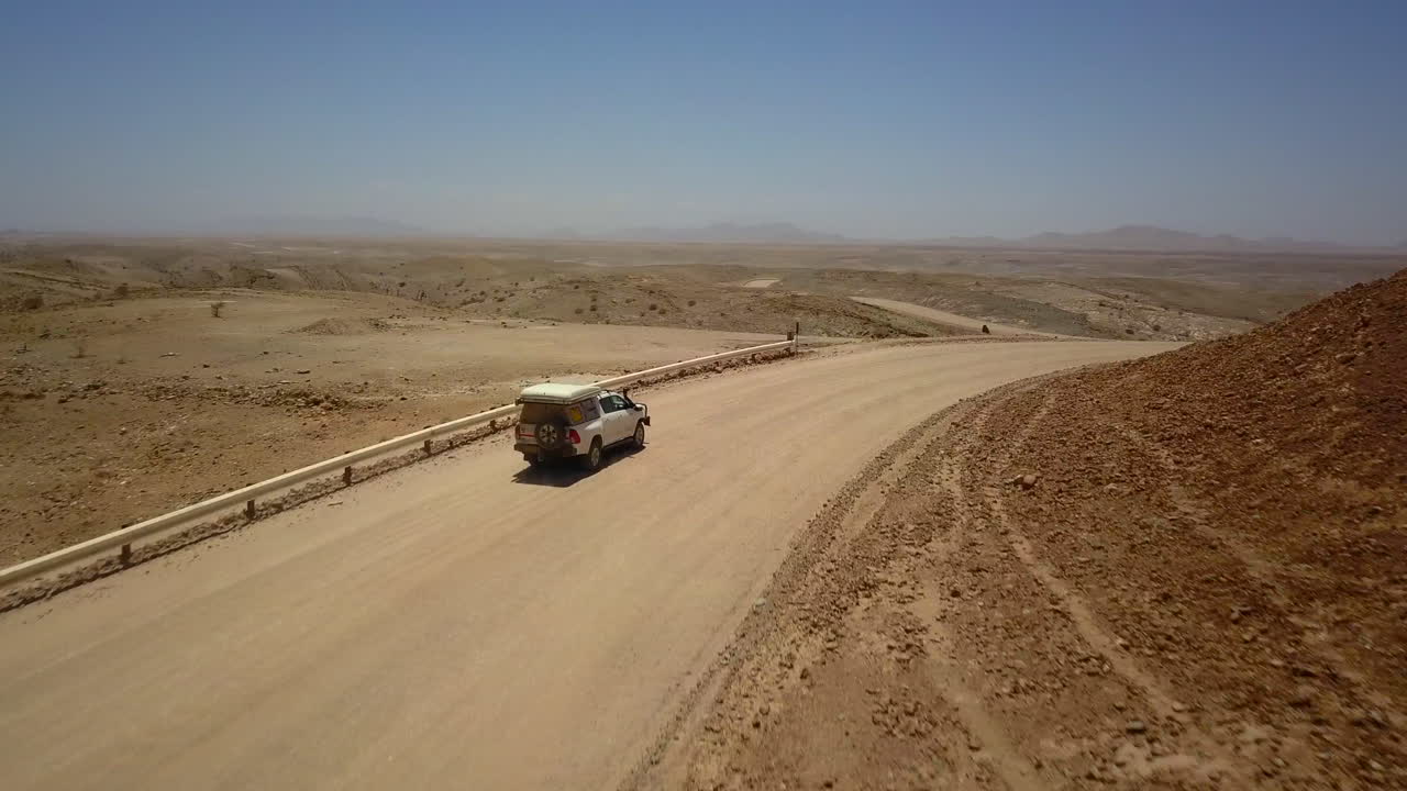 4K footage of a jeep driving along a dusty road, captured from a drone following the vehicle. The breathtaking rocky landscape and expansive views highlight the rugged terrain and adventure journey.