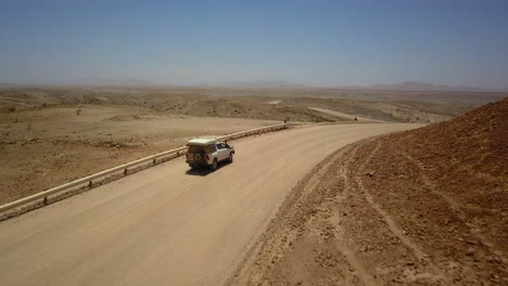 4k footage of a jeep driving along a dusty road, captured from a drone following the vehicle. the breathtaking rocky landscape and expansive views highlight the rugged terrain and adventure journey.