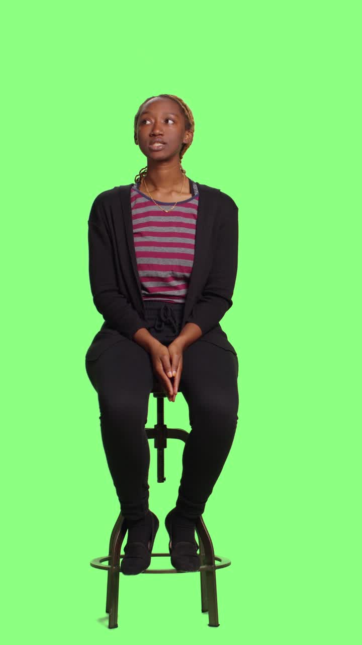 Vertical video: Casual person sitting on chair in studio over full body greenscreen backdrop