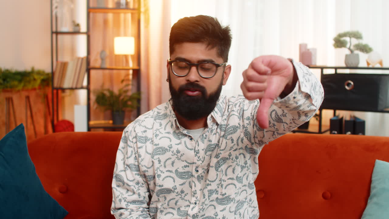 Indian man with angry face shows thumbs down gesture at home expressing disapproval frustration