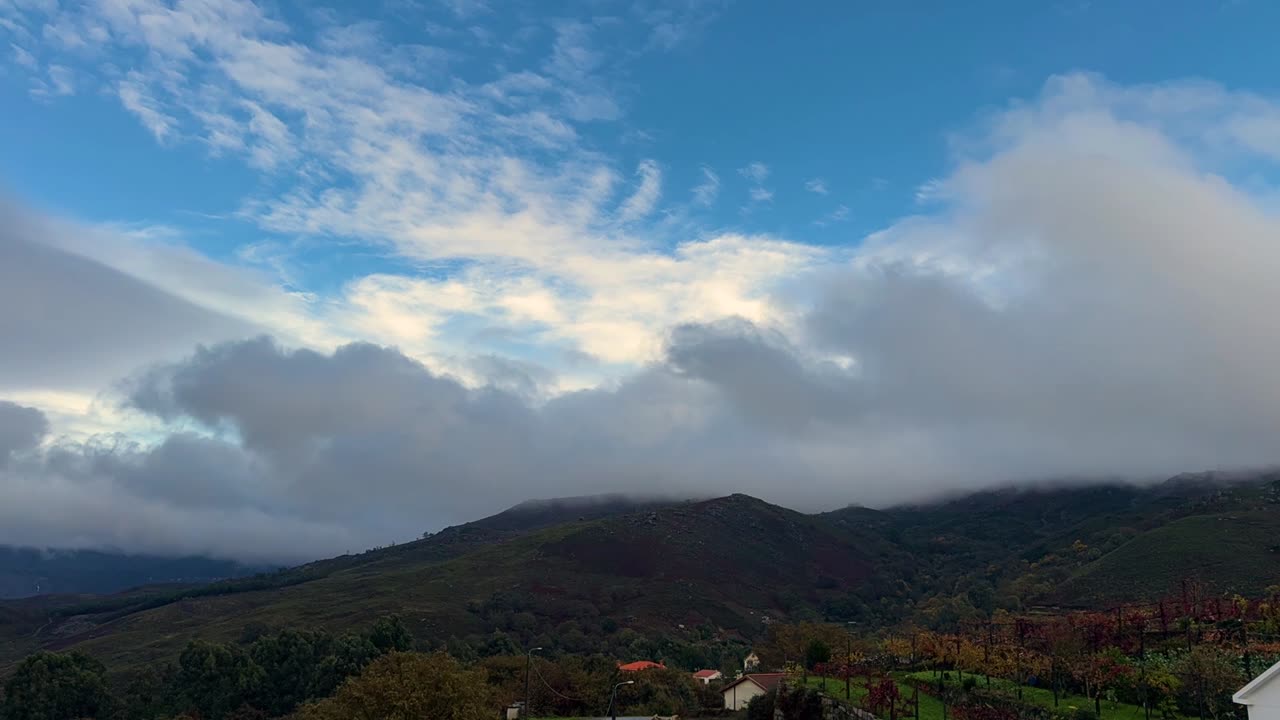 Misty clouds drift over the mountain tops under a blue sky