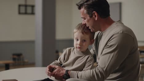 father comforting and calming his young son while sitting on his lap in a restaurant, sharing a tender moment filled with affection, care, and emotional connection during family time