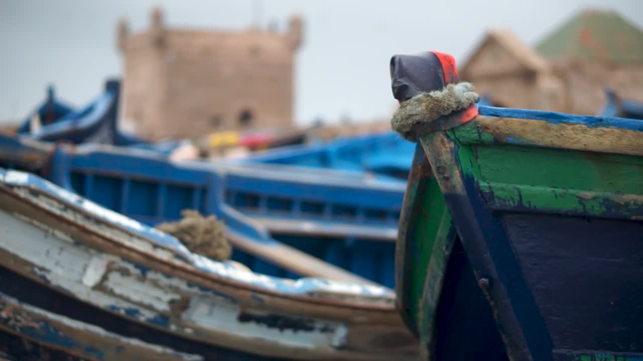 Camera slides to left, prow of fishing boat is in focus and fortress is out of focus