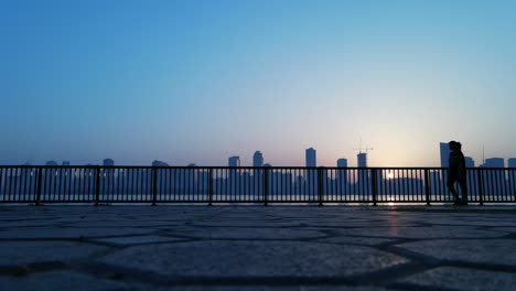 Slow-Motion-Silhouette:-A-woman-exercising-walking-with-a-city-skyline-in-the-background-during-sunrise-in-Sharjah,-United-Arab-Emirates