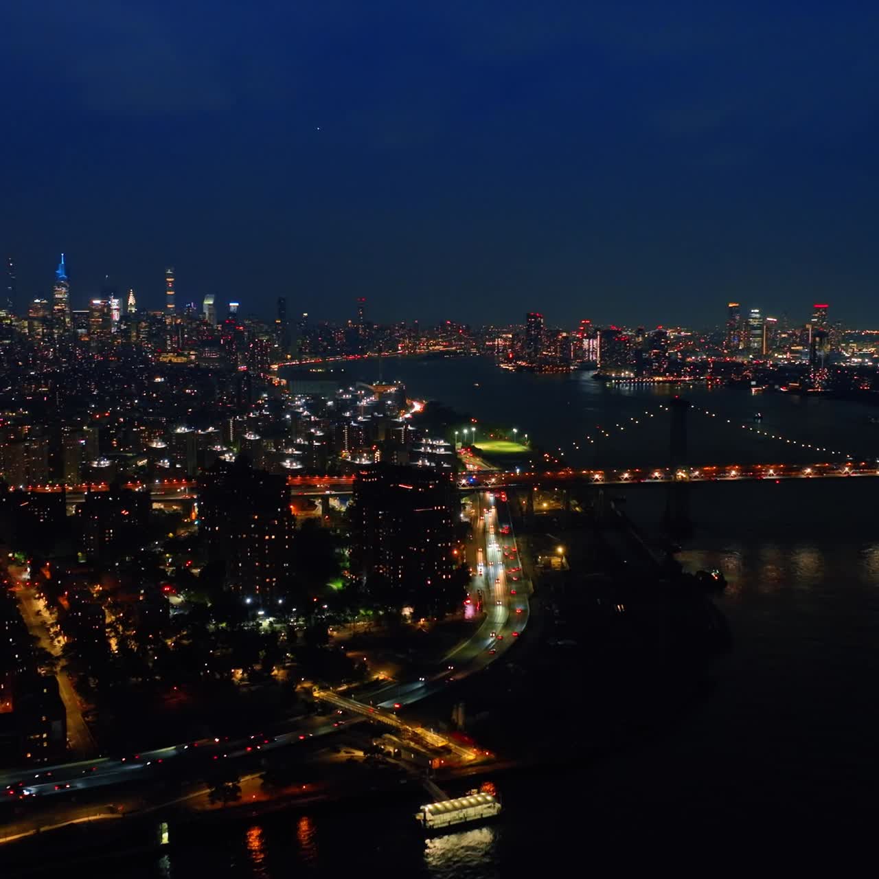 Footage above the dark waters of the East River at night. Luminous cityscape of New York from aerial perspective