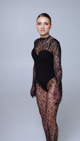 beautiful caucasian woman wearing black lace outfit. model in body stocking long sleeve suit posing in studio. vertical video.