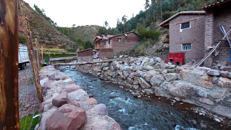 a shot of a house on the side of a stream near a few small adobe houses in peru