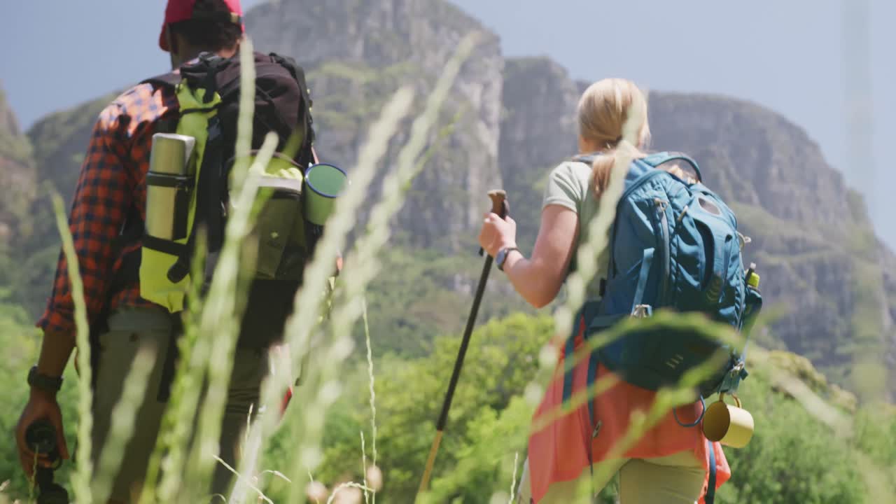 pareja diversa caminando con mochilas y palos de senderismo en las montañas, cámara lenta