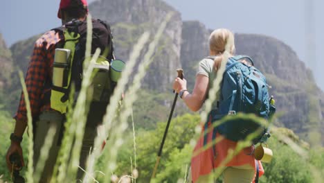 pareja diversa caminando con mochilas y palos de senderismo en las montañas, cámara lenta