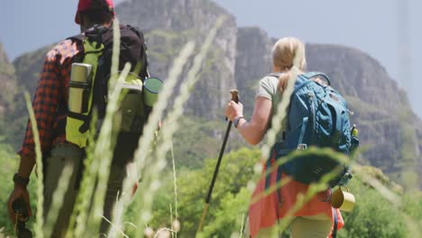 diverse couple hiking with backpacks and hiking sticks in mountains, slow motion