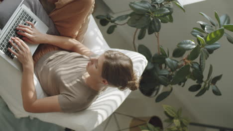 woman sitting in armchair and using laptop at home