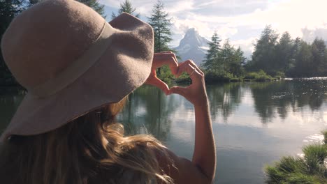 slow motion: young woman on a hike makes heart shaped finger frame in nature