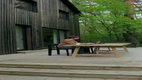 man working on a laptop on a wooden deck outside of a cabin in the forest