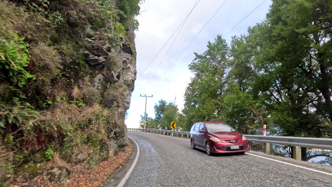 Vehicle travels curving mountain road through lush forest, daylight, smooth camera motion, scenic landscape