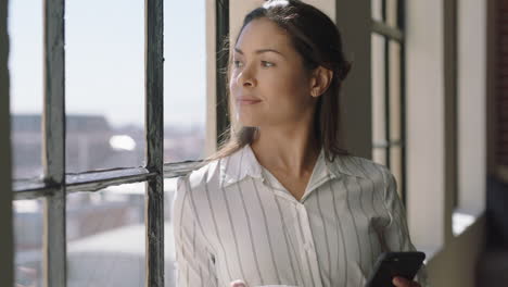 Hermosa-Mujer-Hispana-Usando-Un-Teléfono-Inteligente-Bebiendo-Café-En-Casa-Disfrutando-De-Una-Mañana-Relajada-Navegando-Mensajes-Mirando-Por-La-Ventana-Pensando-Contemplativamente