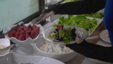 Nahaufnahme-Von-Händen-An-Der-Salatbar,-Die-Essen-Auf-Den-Teller-Legen