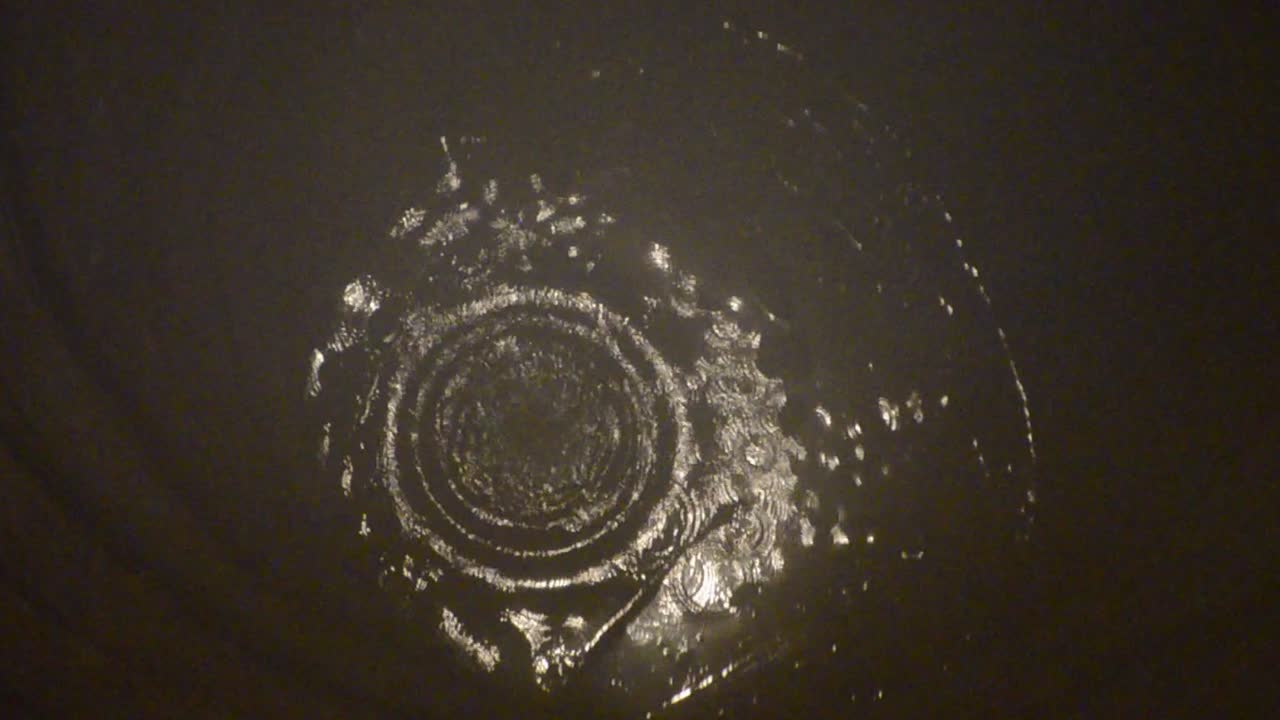 깊은 중세 돌 우물 아래로 떨어지는 바위가 물을 튀기고 바닥에서 반사되는 빛으로 잔물결과 파도를 만듭니다.