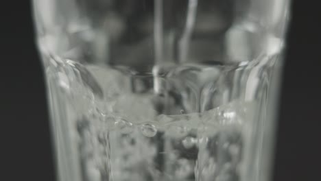 slowmotion closeup of still water pouring into clear glass in front of dark background