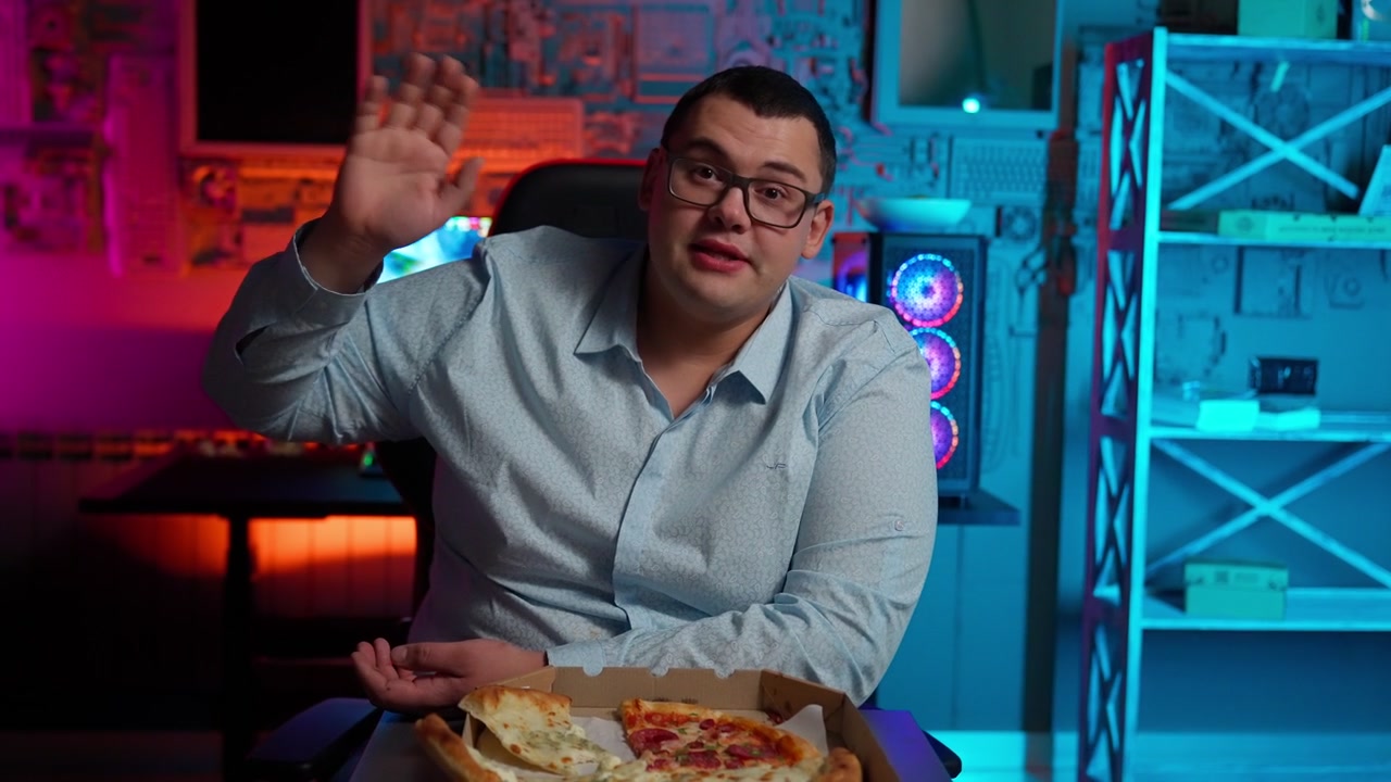 Uomo che saluta e sorride con una pizza in una sala giochi illuminata al neon.