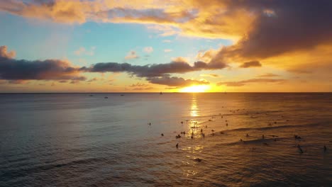 lineup of surfers catching sets of waves at sunset on famous waikiki beach, dawn patrol with tourists and swells in honolulu, hawaii