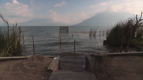 peaks of the three giants volcanos in guatemala hidden in clouds with calm water of lake atitlan in foreground