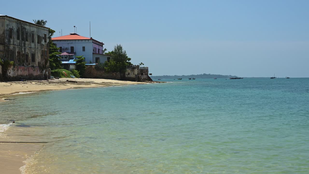 playa tropical y océano en zanzíbar con hermosa agua de mar azul turquesa cristalino, edificios antiguos y idílica playa de arena con cielo azul claro en un día soleado en tanzania, áfrica