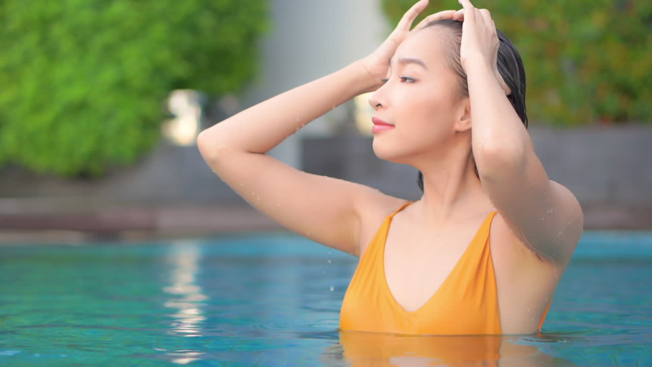 그녀의 젖은 머리를 만지고 수영장에서 아름다운 아시아 여자는 풀 프레임 슬로우 모션을 닫습니다