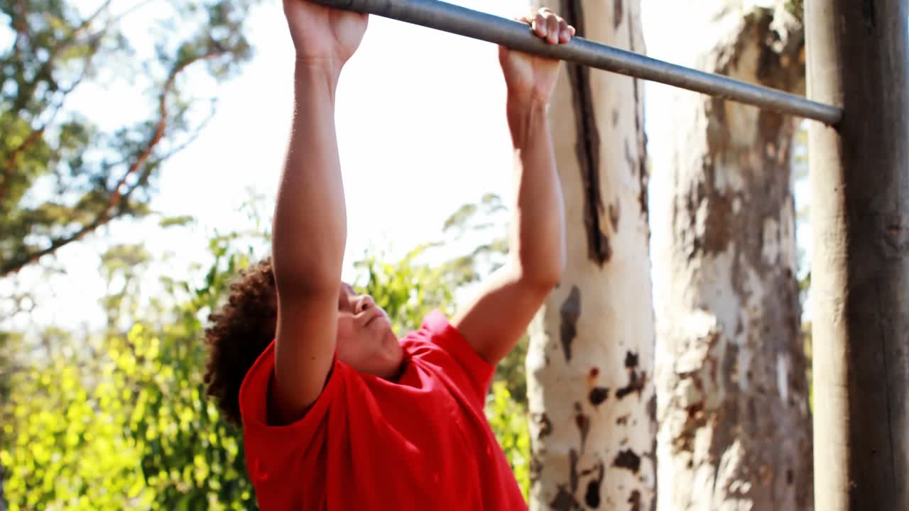 niño realizando pull-ups en la barra durante una carrera de obstáculos